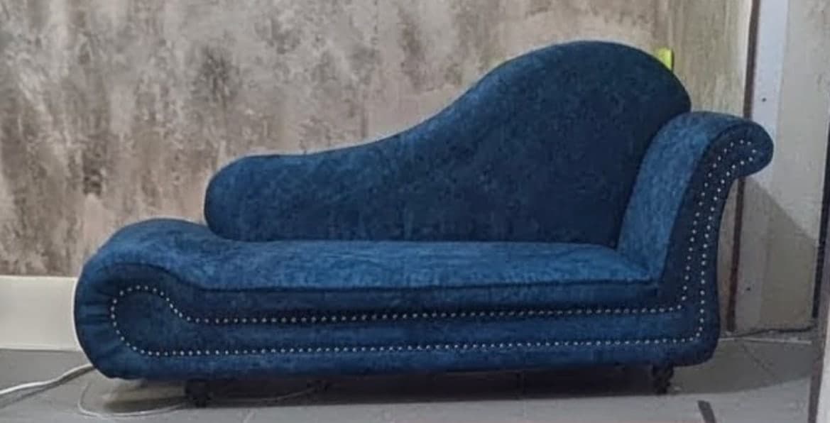 Blue velvet chaise longue with a scrolled back and studded trim along the edges.