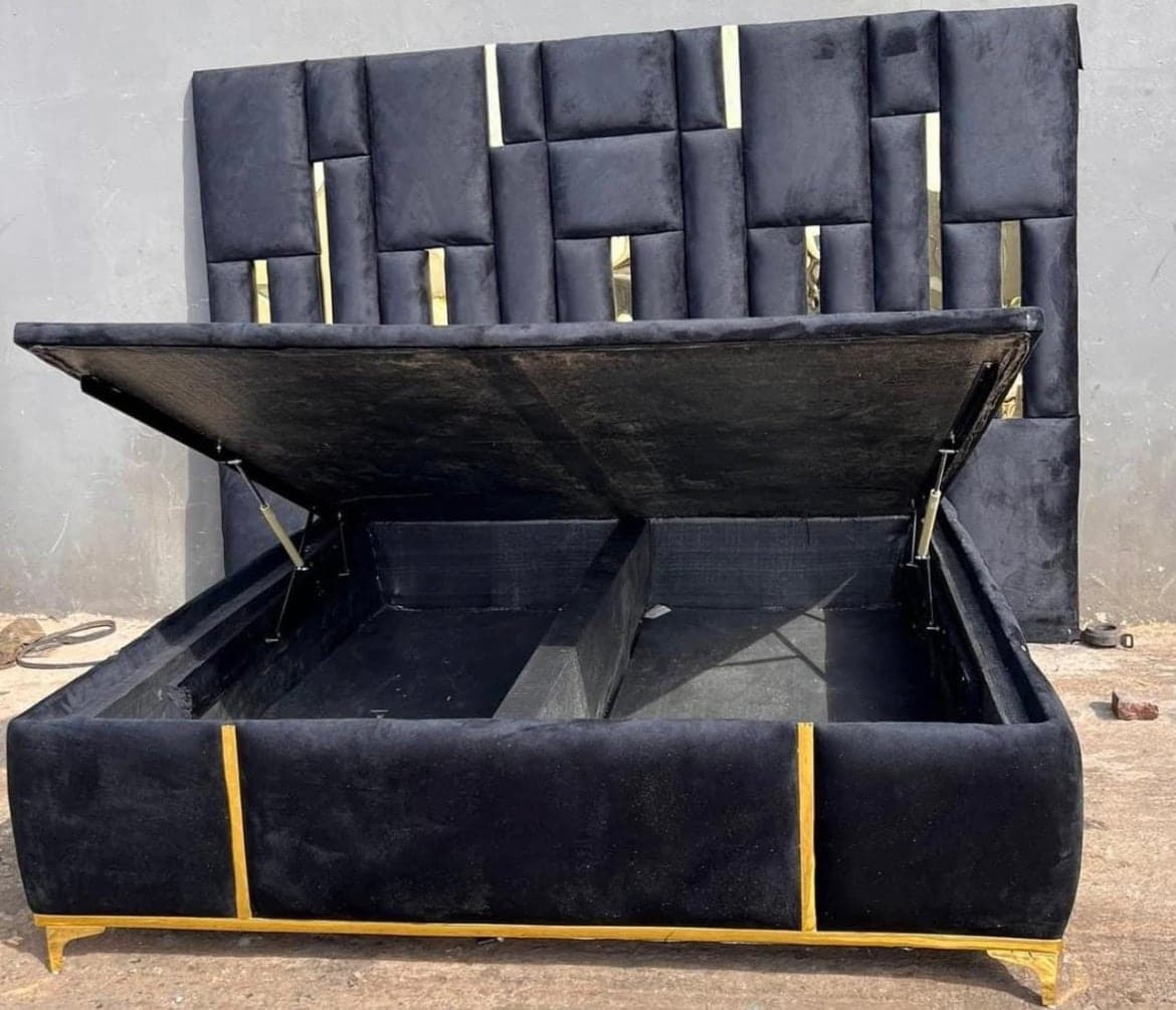 Black velvet headboard of tall panels set with gold inserts, above a lift-up storage base shown open, on gold trim.