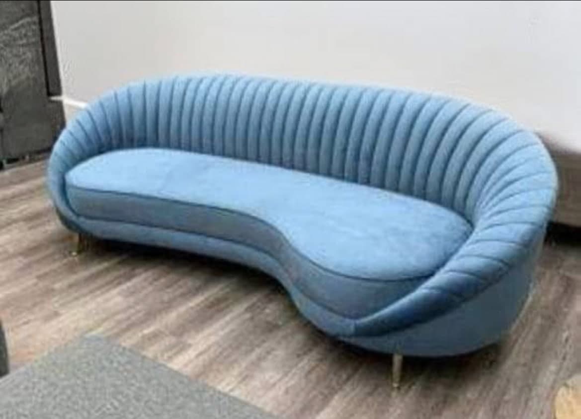 Curved channel-tufted sofa in dusty blue, raised on slim gold legs.