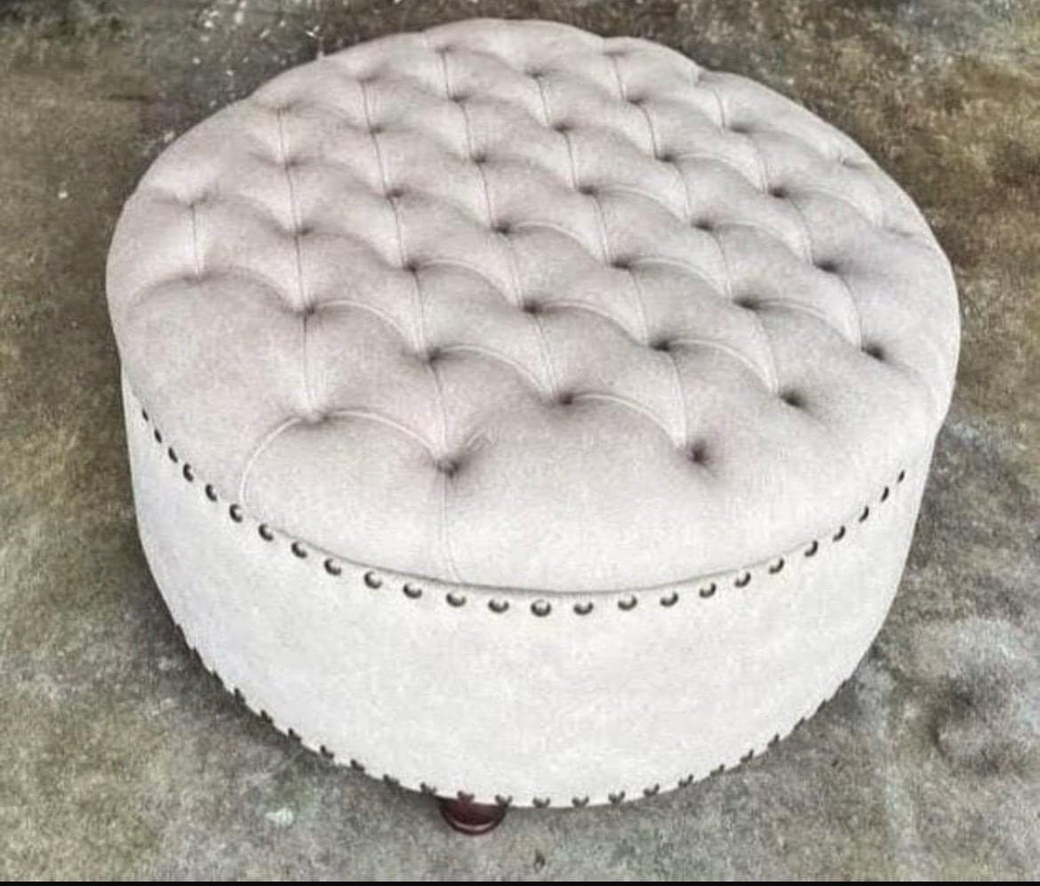 Round ottoman in pale grey velvet, deeply buttoned across the top with studded trim around the base.