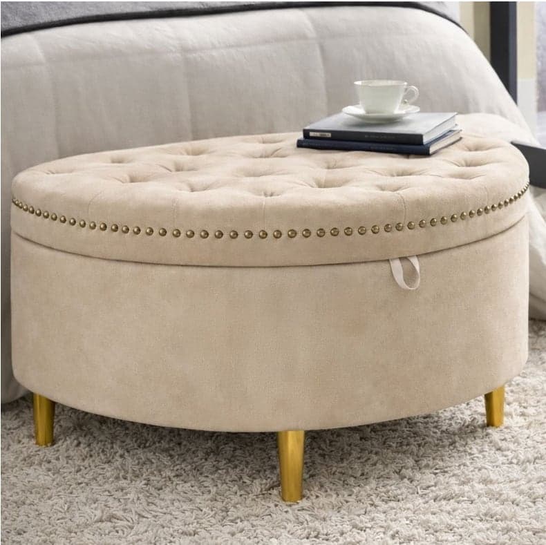 Round cream ottoman with a buttoned lid, studded trim and four tapered gold legs.