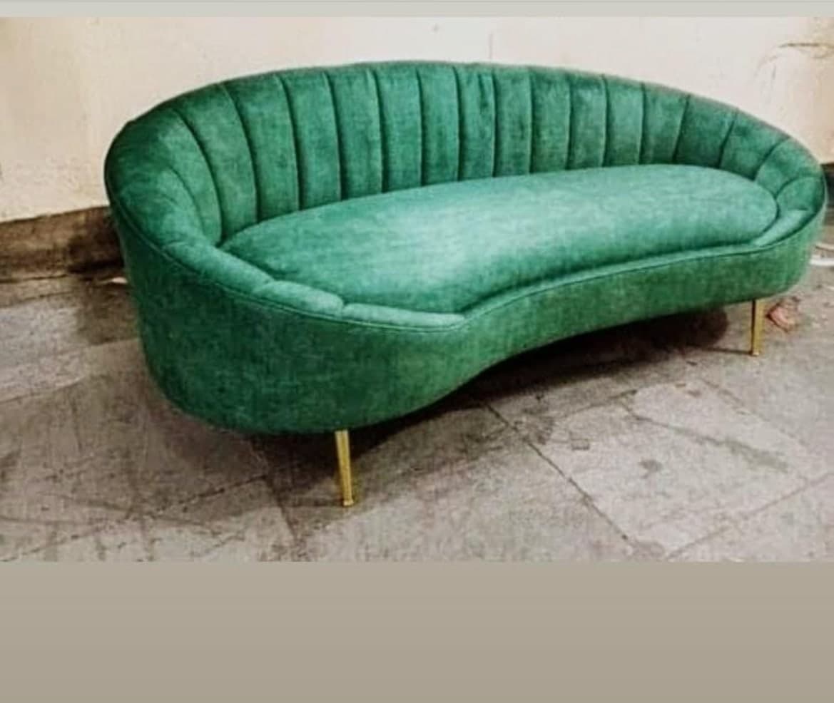 Curved channel-tufted sofa in emerald green, raised on slim gold legs.