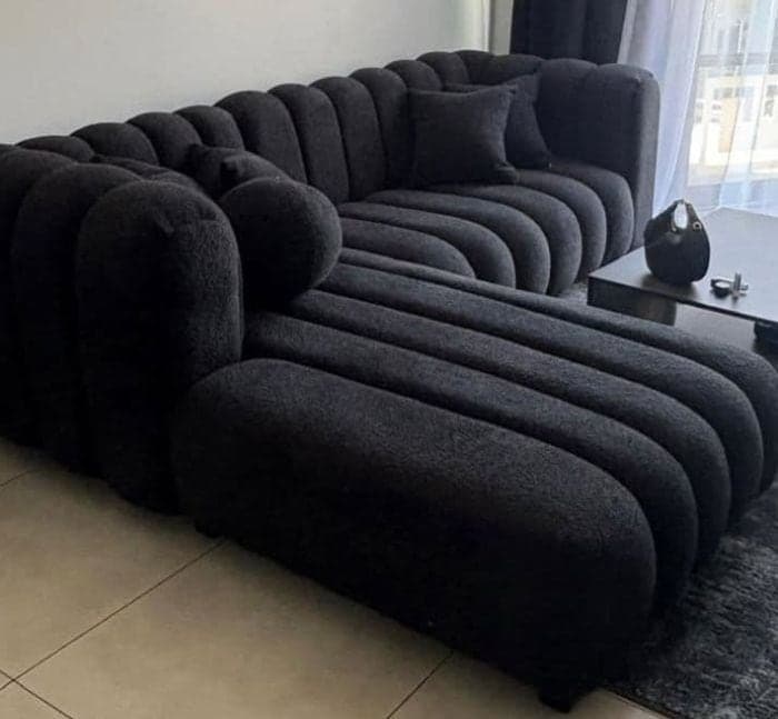 L-shaped black bouclé sectional with deep channelled seating and a bolster cushion.