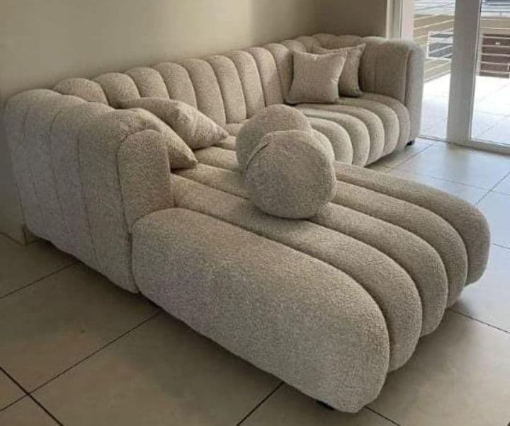 L-shaped bouclé sectional couch in cream, with scatter cushions and a round bolster.