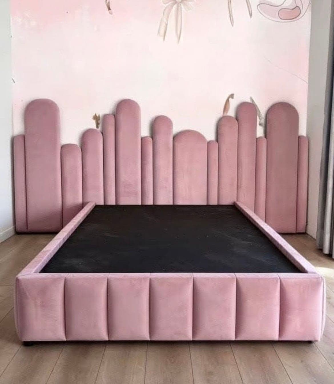 Dusty pink velvet headboard built from rounded panels at staggered heights, above a matching channelled base.